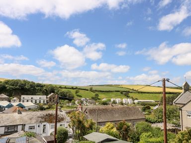 Rooftops of houses with green fields and a blue sky with clouds at Rock Pool House in Porthleven