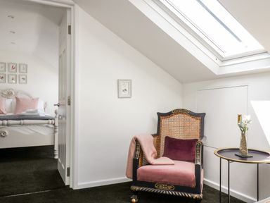 A room with a black and pink armchair a small round table with a vase and flowers and a skylight window at Rock Pool House in Porthleven