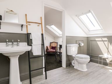 A bathroom with a pedestal sink and toilet next to a doorway leading to a room with chairs at Rock Pool House in Porthleven