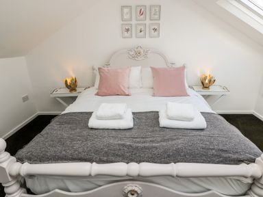 A bedroom with a white bed with pink pillows white towels and bedside tables with lamps at Rock Pool House in Porthleven