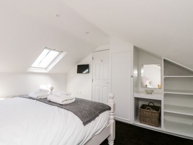 A bedroom with a bed and folded towels under a skylight window with shelves and a mirror at Rock Pool House in Porthleven