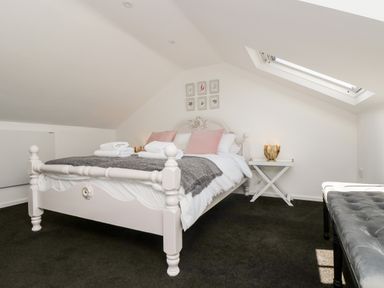 A bedroom with a white bed and pink pillows a side table a skylight window and a black bench at Rock Pool House in Porthleven