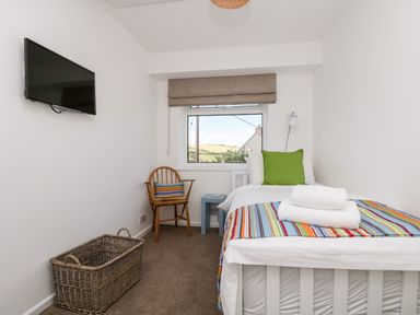 A small bedroom with a single bed a wall-mounted television a wooden chair and a window at Rock Pool House in Porthleven