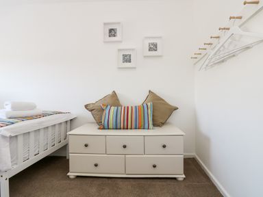 A bedroom with a white bed frame folded towels a chest of drawers with pillows and hangers on the wall at Rock Pool House in Porthleven