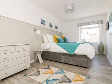 A bedroom with a double bed with colorful pillows a white chest of drawers and a patterned rug at Rock Pool House in Porthleven