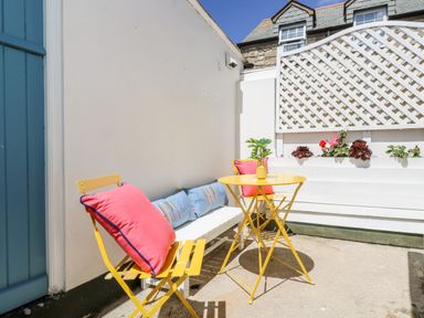 An outdoor patio with yellow chairs and a table with pink and blue cushions and a plant at Rock Pool House in Porthleven