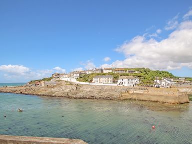 A coastal village with houses on rocky cliffs above clear water under a blue sky at Rock Pool House in Porthleven
