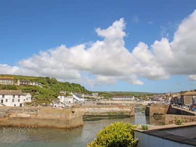A harbor with stone walls surrounded by buildings and greenery under a blue sky at Rock Pool House in Porthleven