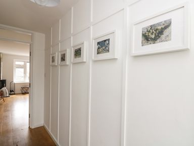 A hallway with five framed pictures on the wall and wooden flooring at Rock Pool House in Porthleven