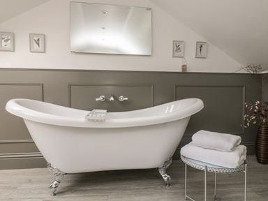 A white clawfoot bathtub in a bathroom with a towel on a small round table and framed pictures on the wall at Rock Pool House in Porthleven