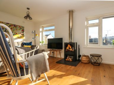 A living room with a fireplace a television a rocking chair and a sofa at Rock Pool House in Porthleven