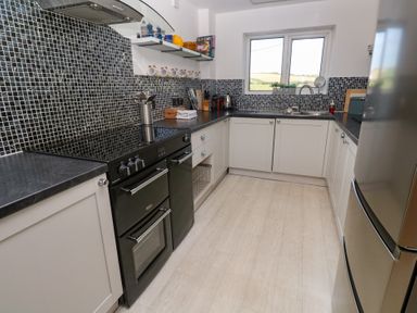 A kitchen with black appliances white cabinets black countertops mosaic tile backsplash and a window at Rock Pool House in Porthleven