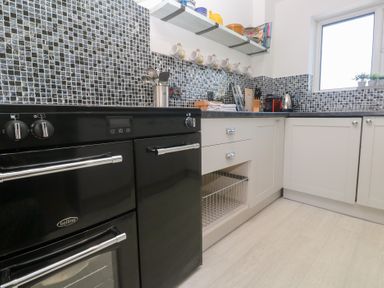A kitchen with black oven white cabinets mosaic tile backsplash and utensils on countertop at Rock Pool House in Porthleven