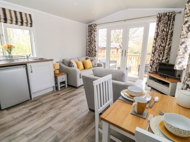 A kitchen and living area with a dining table set for two a sofa armchair and television at Dove Lodge Highampton near Sheepwash