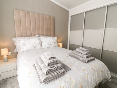 A bedroom with a double bed folded towels on the bed bedside tables with lamps and a wardrobe with sliding doors at Dove Lodge Highampton near Sheepwash
