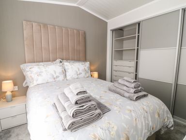 A bedroom with a bed and floral bedding two bedside lamps and an open closet at Dove Lodge Highampton near Sheepwash