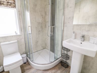A bathroom with a corner shower enclosure toilet sink and small storage rack at Dove Lodge in Highampton near Sheepwash