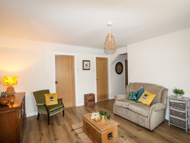 A living room with armchair and sofa around a wooden chest table at Plas Coch Rhoscolyn in Rhoscolyn