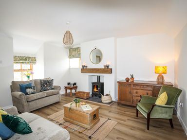 A living room with two sofas a green armchair wooden chest coffee table wood stove and wooden sideboard at Plas Coch Rhoscolyn in Rhoscolyn