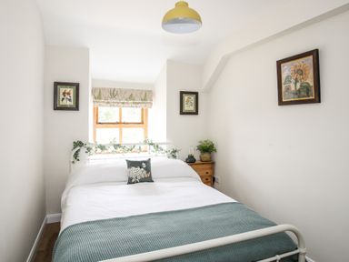 A bedroom with a white metal bed frame a wooden nightstand and floral paintings on the walls at Plas Coch Rhoscolyn in Rhoscolyn