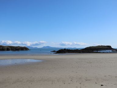 A sandy beach with rocky outcrops and calm sea under a clear blue sky at Plas Coch Rhoscolyn in Rhoscolyn