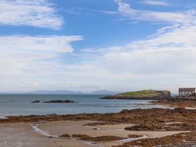 A rocky beach with water and small island near a house at Plas Coch Rhoscolyn