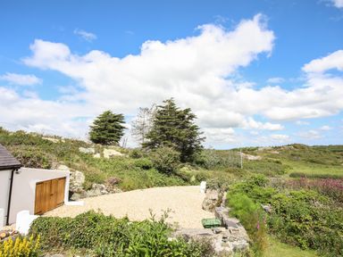 A gravel area next to a garage door with trees and shrubs in the background at Plas Coch Rhoscolyn
