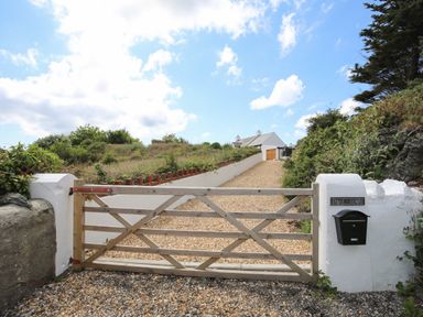 A wooden gate with a mailbox and a gravel driveway leading to a house at Plas Coch Rhoscolyn