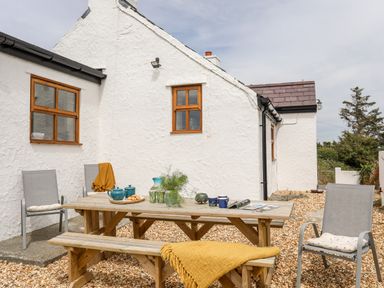 An outdoor patio area with a wooden picnic table and benches surrounded by gravel at Plas Coch Rhoscolyn in Rhoscolyn