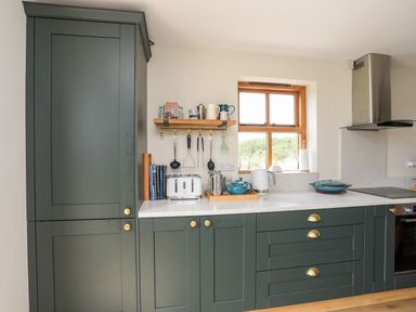 A kitchen with green cabinets a white countertop a window kitchen utensils and appliances at Plas Coch Rhoscolyn in Rhoscolyn