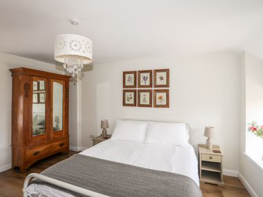 A bedroom with a double bed bedside tables lamps a wooden wardrobe and framed pictures on the wall at Plas Coch Rhoscolyn in Rhoscolyn