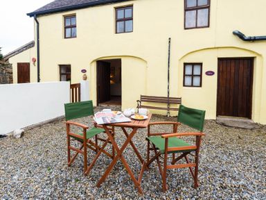 An outdoor seating area with two chairs and a table set with breakfast items in front of a yellow building at The Stable in Fethard-On-Sea County Wexford
