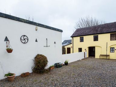 An outdoor courtyard with a yellow building a white wall hanging pots and plants at The Stable in Fethard-On-Sea County Wexford
