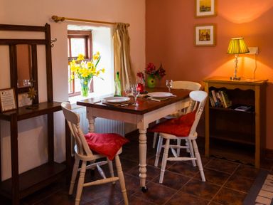 A dining area with a wooden table set for two and white chairs with red cushions at The Stable in Fethard-On-Sea County Wexford