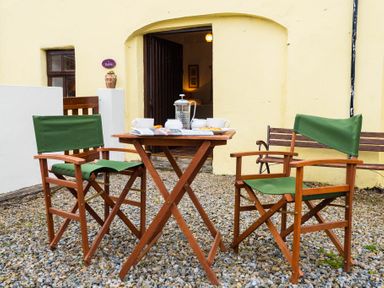 An outdoor seating area with two wooden chairs with green fabric and a wooden table set for tea at The Stable in Fethard-On-Sea County Wexford