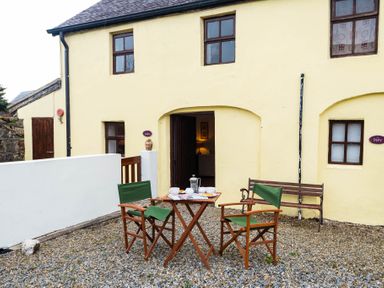 An outdoor patio area with two green canvas chairs and a wooden table with tea set in front of a yellow building at The Stable in Fethard-On-Sea County Wexford