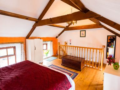 A bedroom with a red bedspread wooden beams a white wardrobe a wooden chest and a mirror at The Stable in Fethard-On-Sea County Wexford