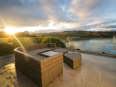 An outdoor patio with wicker seating and glass railing overlooking a body of water at Kessock in Bowness-On-Windermere