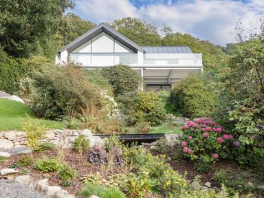 A modern house with a glass balcony surrounded by a garden with various plants and flowers at Kessock in Bowness-On-Windermere