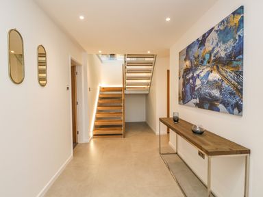 A hallway with wooden stairs a table with glass decor two mirrors and abstract painting at Kessock in Bowness-On-Windermere