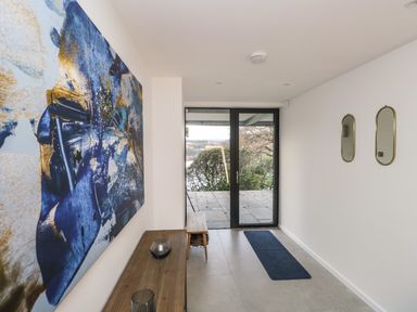 A hallway with abstract blue and gold artwork a wooden table and bench near glass doors and two oval mirrors on the wall at Kessock in Bowness-On-Windermere