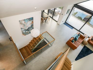 A modern living room with brown leather sofas near large windows overlooking water at Kessock in Bowness-On-Windermere