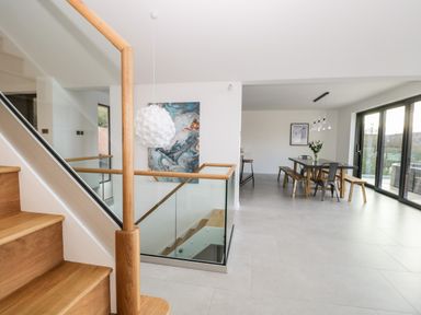 A staircase with wooden handrails and glass panels next to a dining area with a table, benches, chairs, and sliding glass doors at Kessock Bowness-On-Windermere