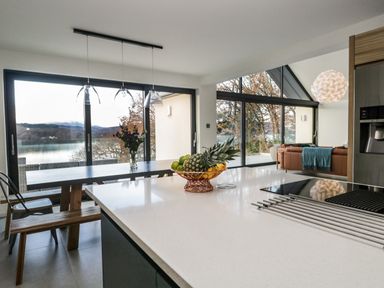 A kitchen island with fruit bowl and stovetop in a room with dining table and large windows at Kessock in Bowness-On-Windermere