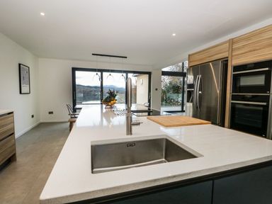 A kitchen with a sink on an island countertop and a view of a lake through large windows at Kessock in Bowness-On-Windermere