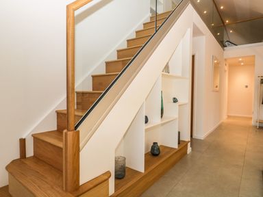 A hallway with wooden stairs and built-in white shelves under the stairs containing decorative glass items at Kessock in Bowness-On-Windermere