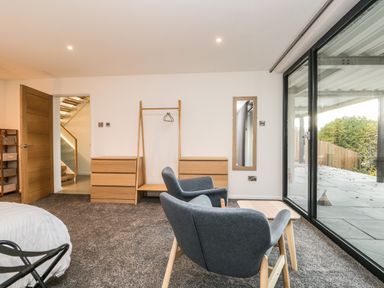 A bedroom with two grey chairs and a small table near sliding glass doors and wooden dressers at Kessock in Bowness-On-Windermere
