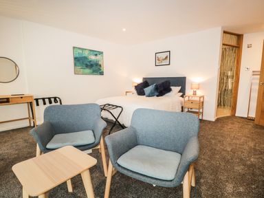 A bedroom with a bed lamps bedside tables two armchairs a small table a desk and a door at Kessock in Bowness-On-Windermere