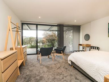 A bedroom with a bed chairs wooden dressers and a large sliding glass door at Kessock in Bowness-On-Windermere