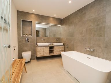 A bathroom with a bathtub toilet double sinks and a wooden bench at Kessock in Bowness-On-Windermere